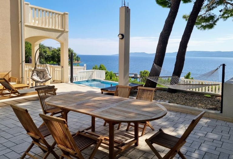 The photo shows a dining table, deck chairs and swings in the central courtyard overlooking the pool and the open sea.