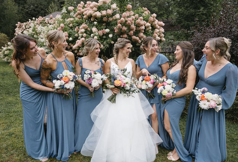 Une mariée et son cortège habillé en bleu se regarde et sourit. Elles tiennent un bouquet de fleurs.