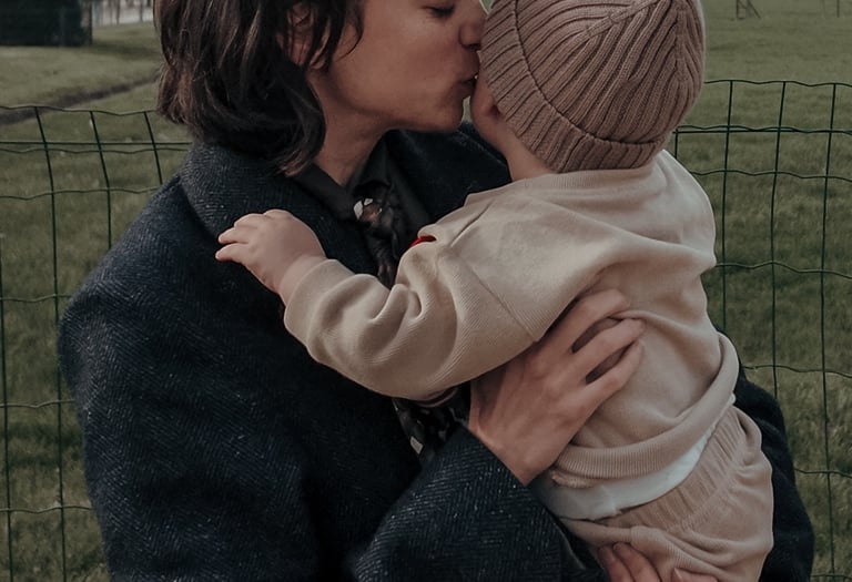 Un parent portant un manteau tient un jeune enfant en tenue beige près de la Tour Eiffel, montrant u