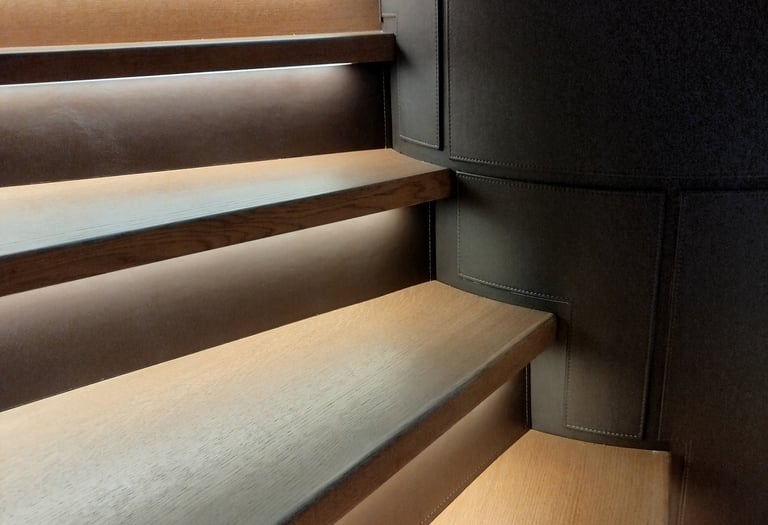 Modern wooden staircase with integrated LED tread lighting and dark leather wall panels.