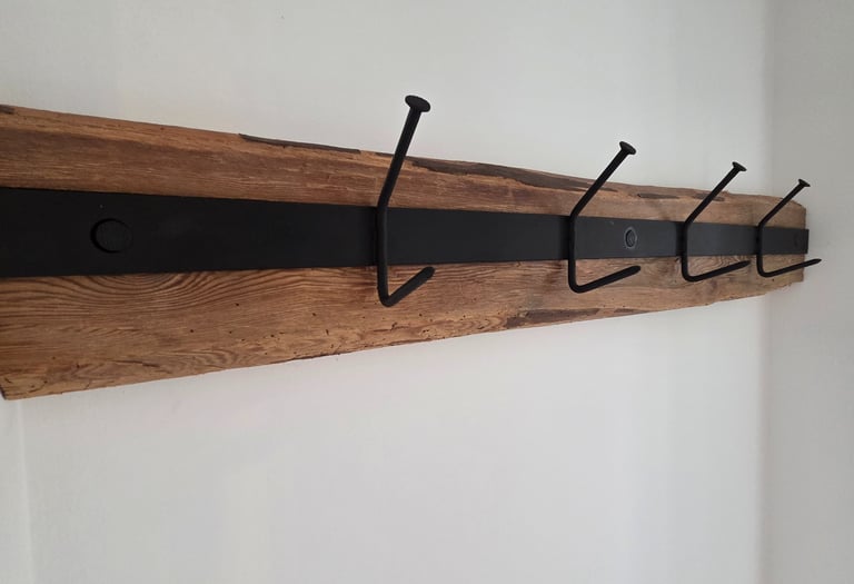 Wandgarderobe aus rustikalem Altholz mit schwarzem Metallband und vier massiven Eisenhaken im Industrial-Look.
