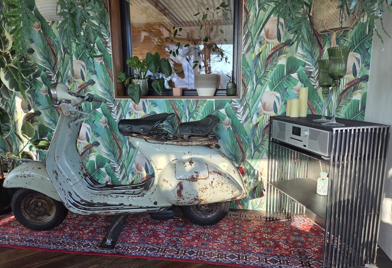 Vintage-Vespa als dekoratives Highlight vor Dschungel-Tapete neben modernem Holz-Sideboard.