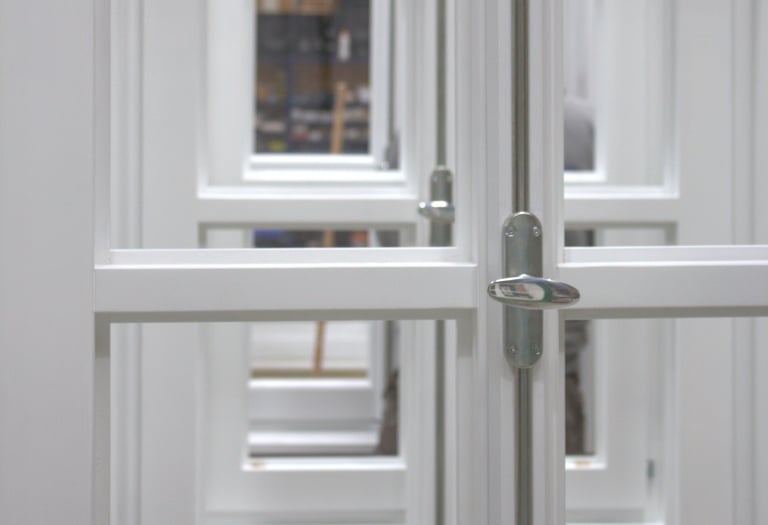 etailaufnahme weiß lackierter Holzfenster mit silbernem Griff und Blick durch mehrere Fensterebenen.