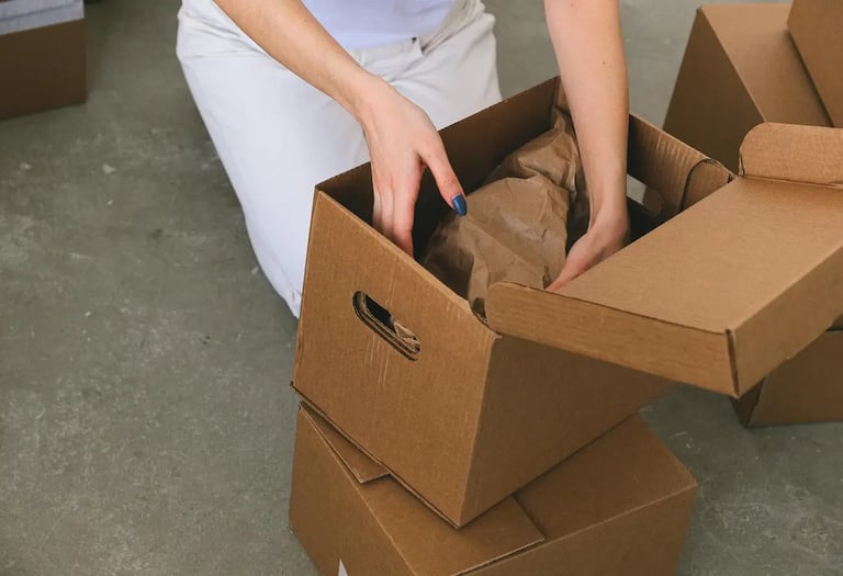 A person packing cardboard shipping boxes with brown paper for safe moving and delivery.