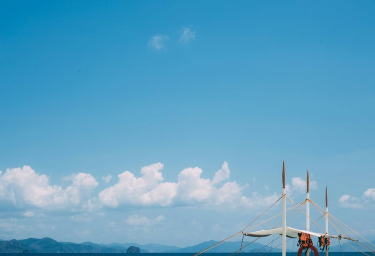 Traditional Filipino outrigger boat on a sereme tropical beach with clear blue water and distant islands under a bright sky