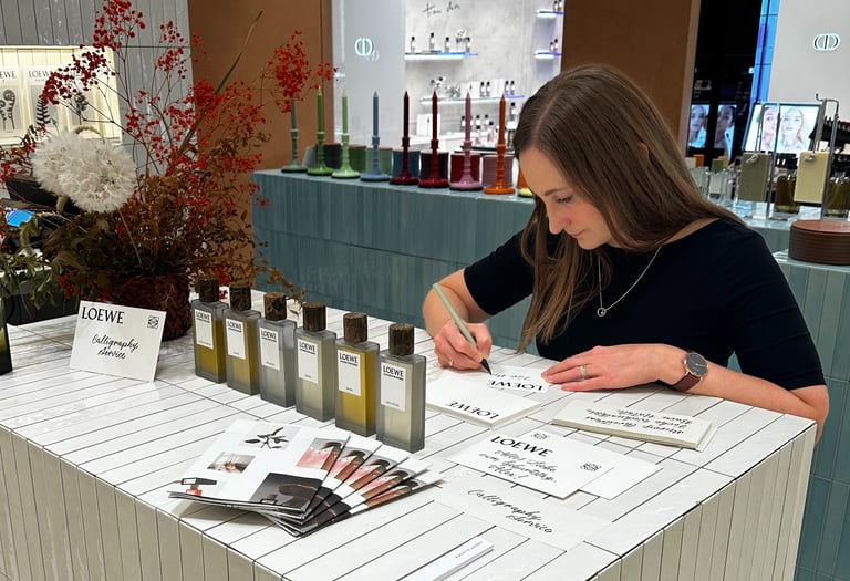 A calligrapher provides hand-lettered personalization for Loewe perfumes at a luxury fragrance counter.