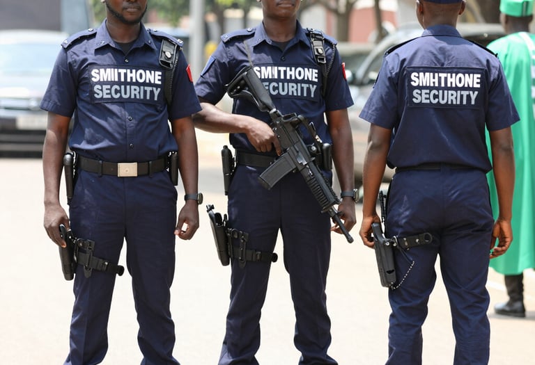 A Nigerian security guard confidently standing beside an electronic gate secured by Smithone Intelligence Ltd.