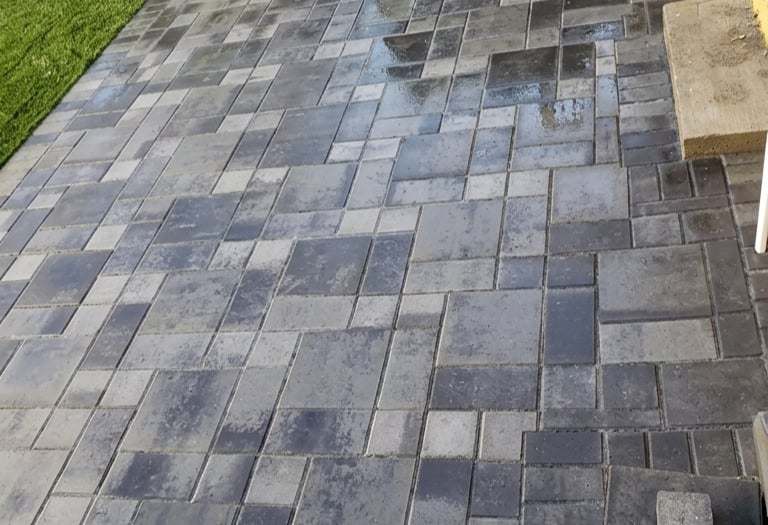 Backyard landscaping with modern grey interlocking pavers and vibrant artificial grass lawn creating