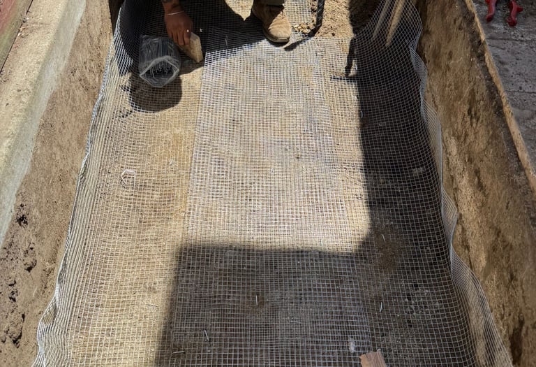 A contractor installs wire mesh hardware cloth in a trench for gopher and rodent proofing a foundation.