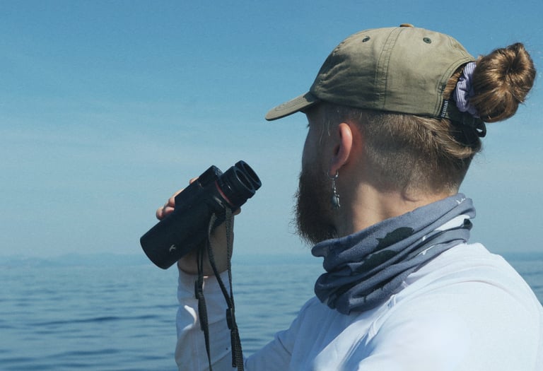 Scientist on a boat at sea using binoculars to spot cetaceans.