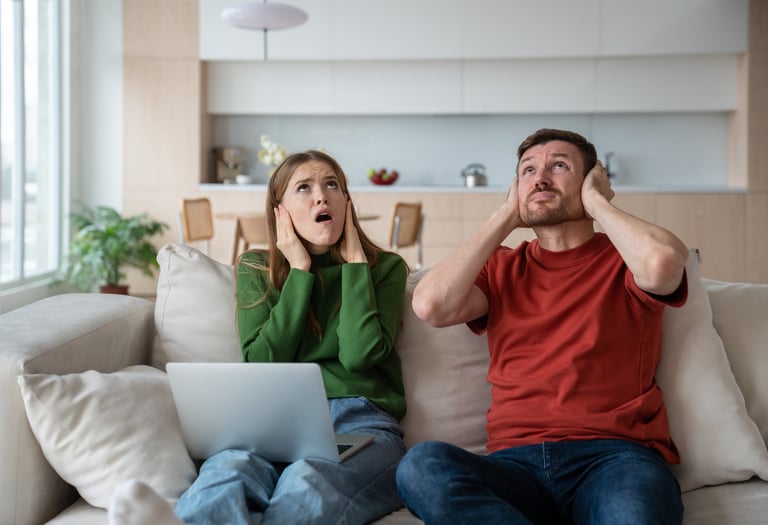 Man and woman cover their ears and look up as they are struggling with noise from upstairs neighbour