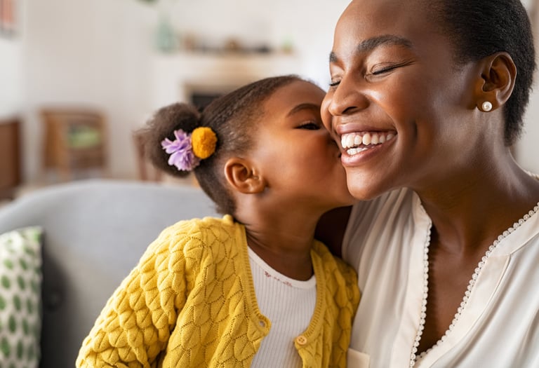 A mother smiles as her young daughter kisses her cheek