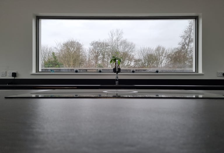 Modern kitchen sink with a chrome faucet in front of a large picture window overlooking a winter forest.