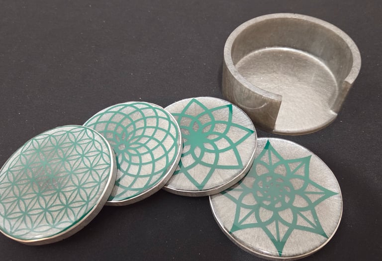 Set of four grey round coasters with green geometric mandala patterns and matching holder.