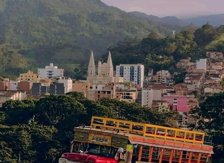 A colorful traditional Chiva bus parked on a mountain road with a scenic Colombian town view.