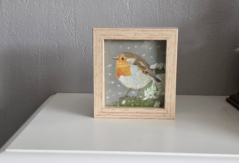 Framed pastel art print of a European robin bird perched in a winter snow scene on a white mantle.