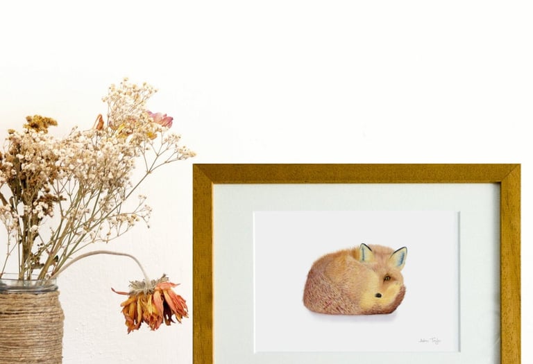 Framed fox art print sitting on a wooden table next to a vase of dried flowers.