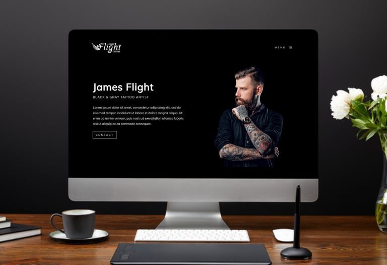a computer screen on a desk featuring the homepage of a tattoo artist website