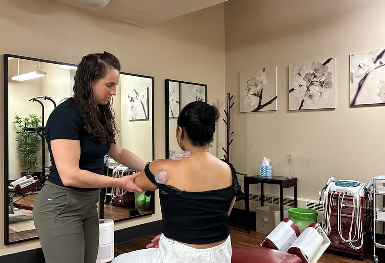 Chiropractor cupping a patient's shoulder and assisting movement with treatment room in background. 