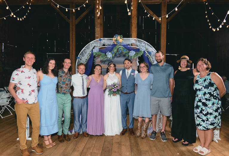a group of people including a bride and groom standing in front of a wedding arch
