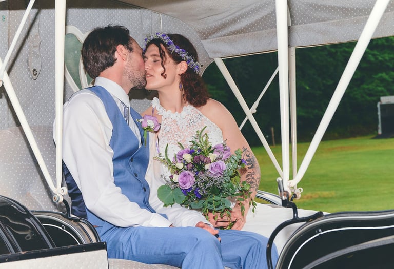 a bride holding a bouquet and groom in blue suit kissing in a carriage