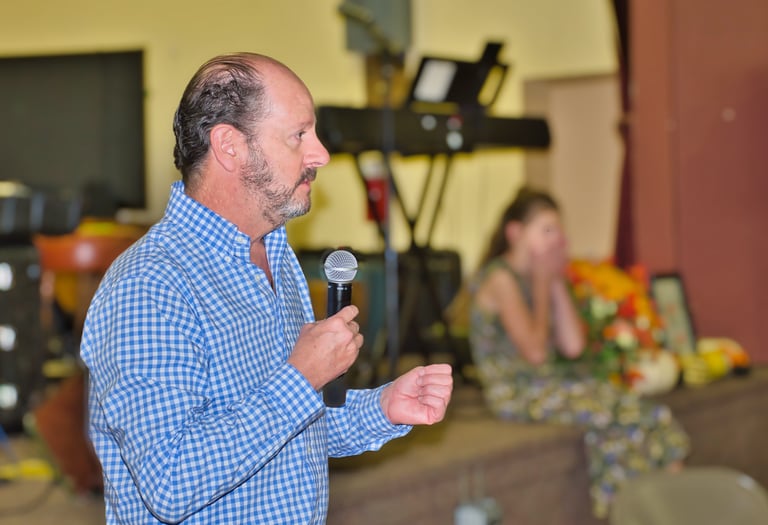 a man in a blue shirt is holding a microphone speaking to the audience