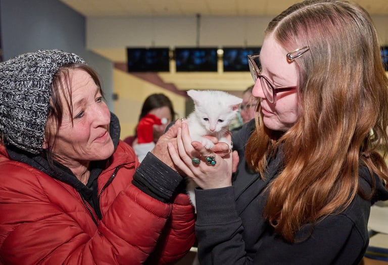 two women holding a white kitten in a room