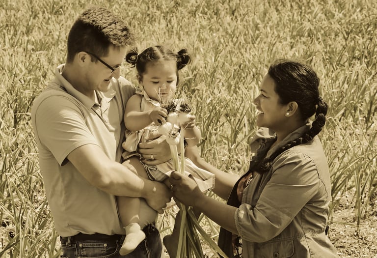 a man and woman holding a baby in a garlic field