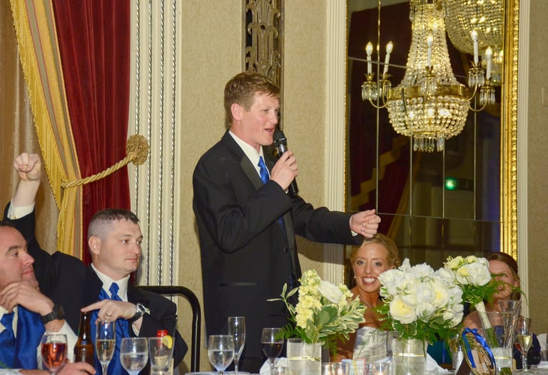 a groom giving a speech to the audience at the head table in a wedding