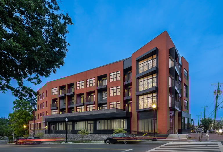 Modern red brick multi-story apartment building with black metal balconies at dusk. 