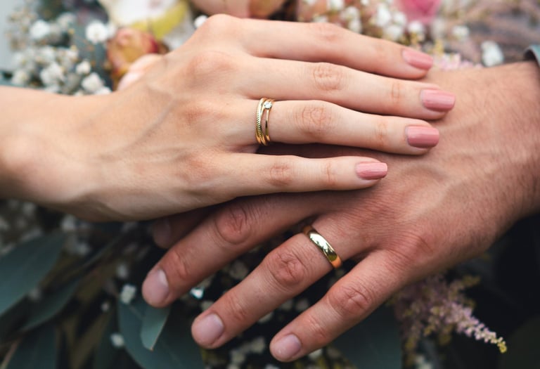 Hände mit Eheringen liegen auf einem Brautstrauß mit rosa Rosen. Detailaufnahme: Just Perspectives.