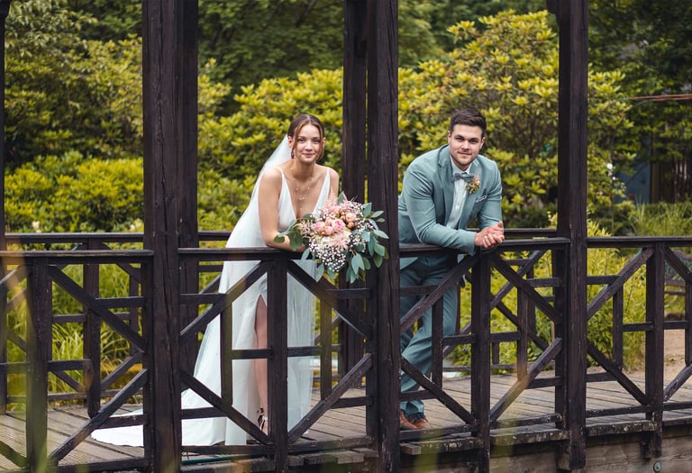 Brautpaar lehnt entspannt an einer Holzbrücke im Grünen. Hochzeitsportrait von Just Perspectives.