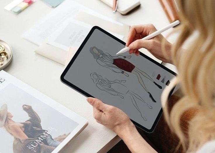 a woman sitting at a table with a tablet and a pen