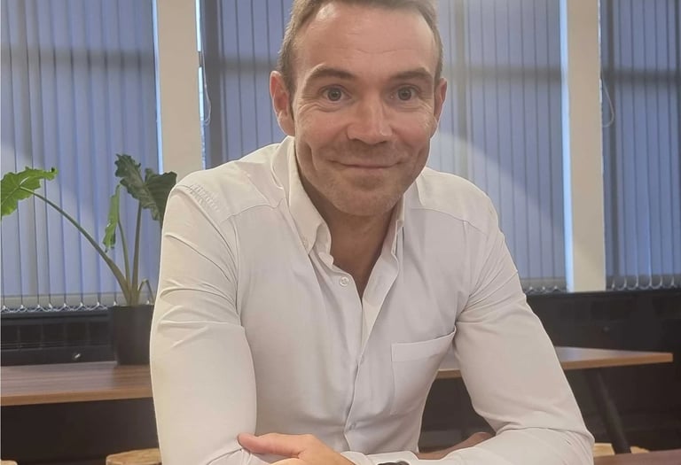 Man in a white shirt looks into the camera with a small smile