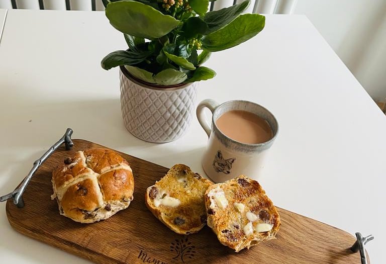 a wooden serving board with hot cross buns and a cup of tea