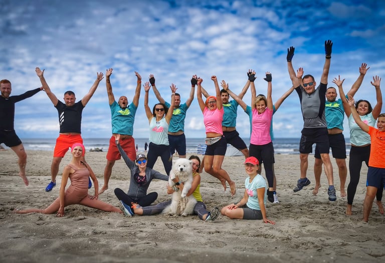 Uśmiechnięta grupa osób w podskoku na plaży po treningu. 