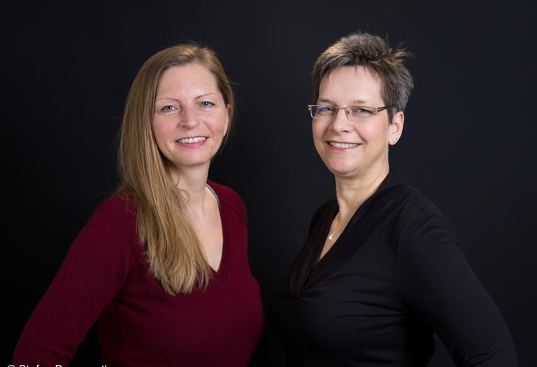 two women standing next to each other in front of a black background