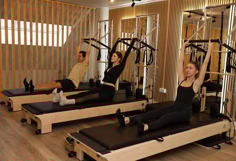 Três pessoas a realizar um exercício de Pilates em reformers torre, puxando a barra push-through