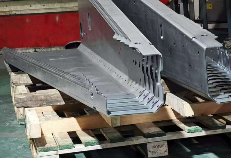 Precision bent galvanized steel sheet metal parts stacked on a wooden pallet in a workshop.