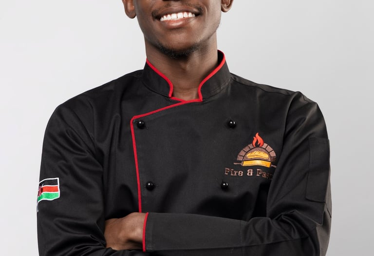 A smiling young chef wearing a professional black double-breasted culinary jacket with red trim.