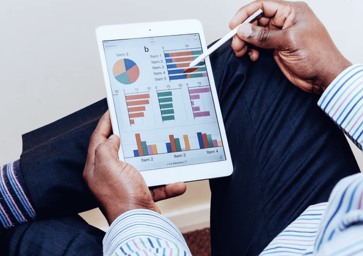 A businessman using a stylus to analyze financial data charts on a digital tablet.