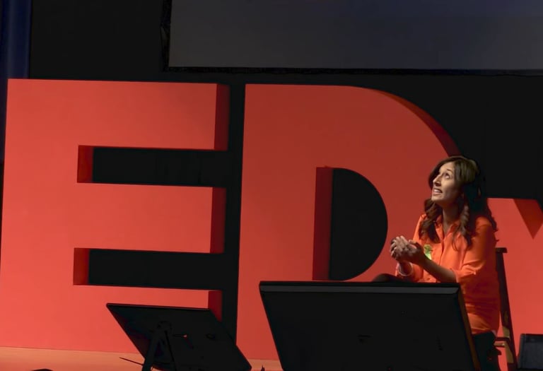 A woman in an orange outfit speaks passionately on stage, with large red "TEDx" letters behind her.