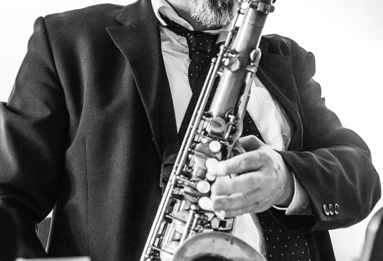 Black and white photo of a male jazz musician in a suit playing the tenor saxophone.