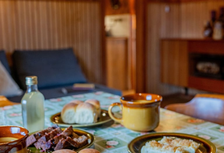 Homemade dinner rolls and pastries served on a floral tablecloth in a rustic wood-paneled dining room.
