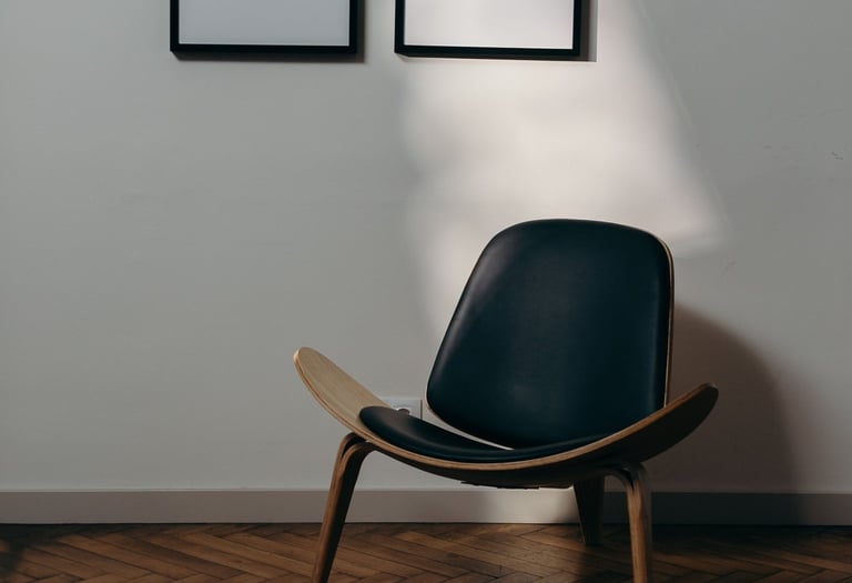 Modern black leather shell chair on herringbone wood floors with blank wall art frames in a minimalist room.