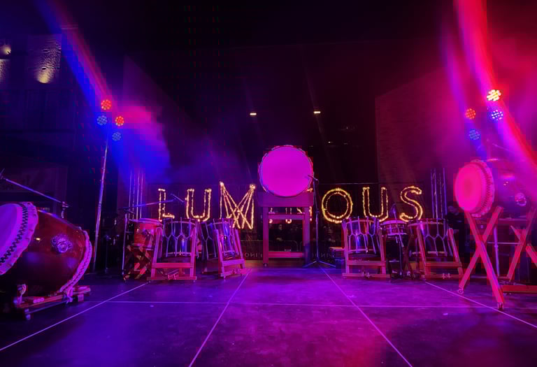 Traditional Japanese Taiko drums on a stage with purple neon lighting and a glowing Luminous sign.