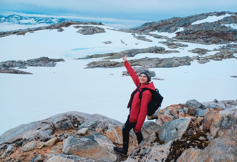A female hiker in a red jacket standing on snowy mountain rocks during a winter trekking in Norway.