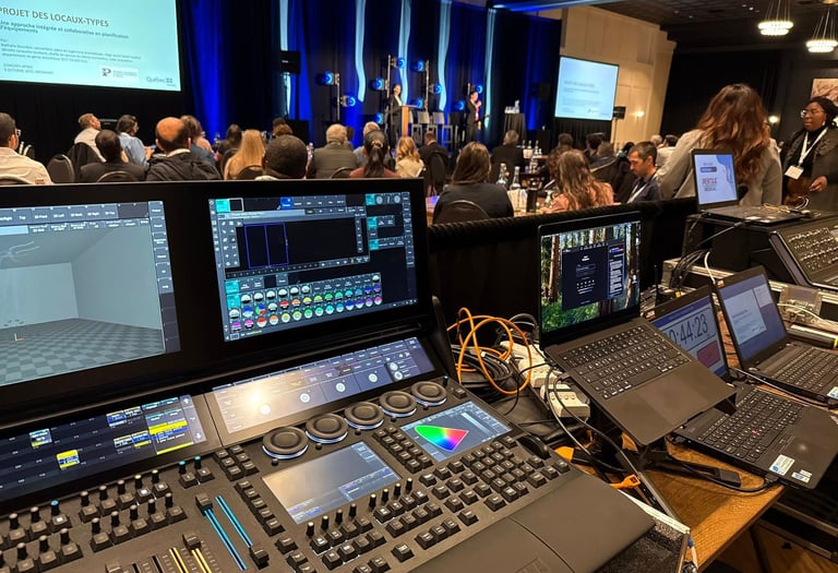 Professional lighting console and laptops at a live event production booth in a conference hall.