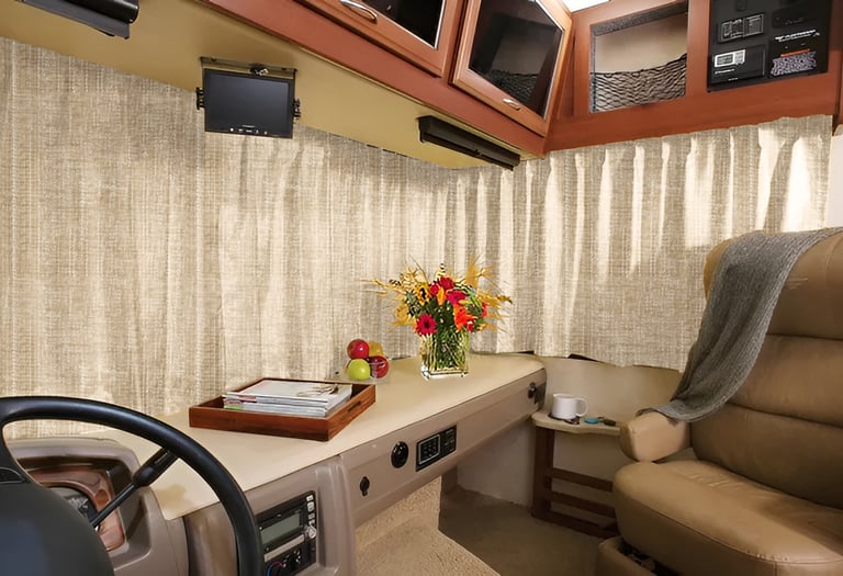 Interior of a luxury RV cockpit featuring beige blackout curtains, a leather swivel chair, and fresh flowers.
