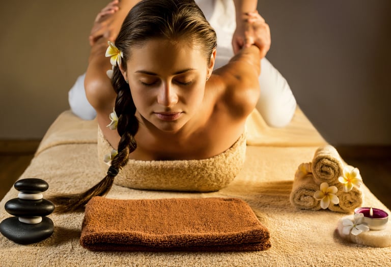 Woman receiving a professional Thai massage at a luxury spa with hot stones and frangipani flowers.